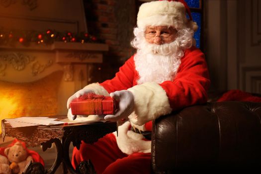 Portrait of happy Santa Claus sitting at his room at home near Christmas tree and reading Christmas letter or wish list.