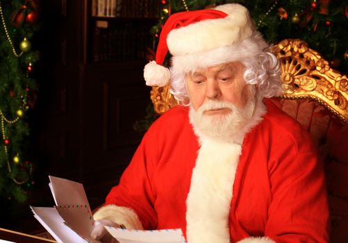 Santa sitting at the Christmas tree, holding Christmas letters and having a rest by the fireplace.