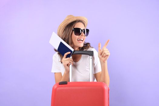 Young tourist girl in summer casual clothes, with sunglasses, red suitcase, passport isolated on purple background