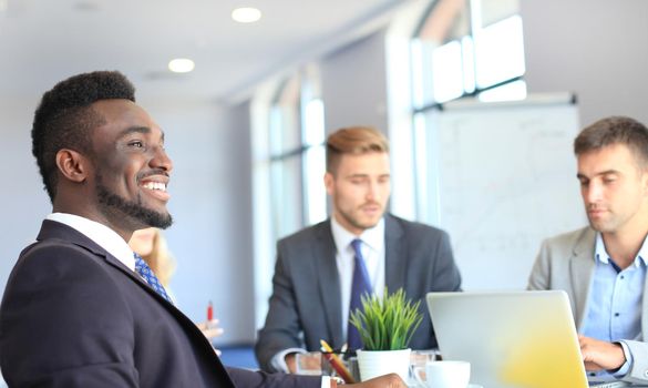 Smiling confident African businessman in a meeting with a colleagues seated at a conference table in the office.