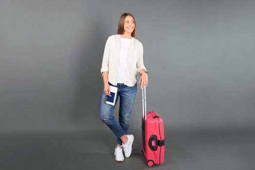 Young tourist girl in summer casual clothes, with sunglasses, red suitcase, passport, tickets isolated grey background.