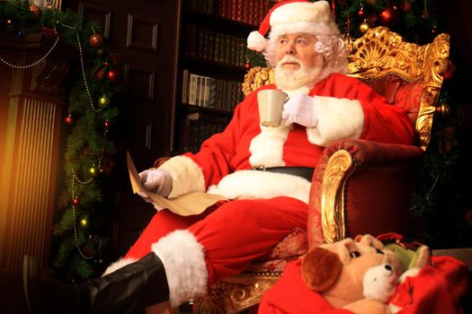 Santa Claus having a rest in a comfortable chair near the fireplace at home.