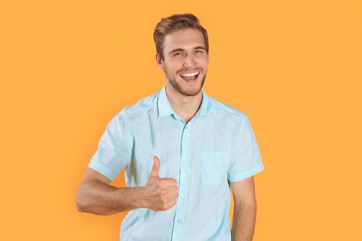 Young man showing thumbs up isolated over yellow background