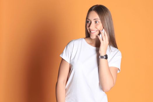 Young woman dressed in basic clothing isolated on yellow background, talking on mobile phone.