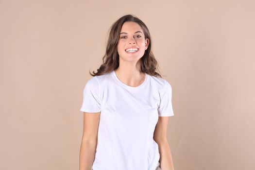 Cheerful brunette woman dressed in basic clothing looking at camera, isolated on beige background