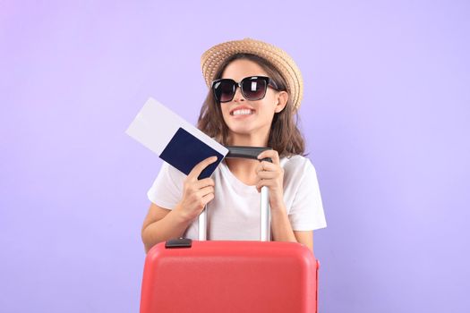 Young tourist girl in summer casual clothes, with sunglasses, red suitcase, passport isolated on purple background