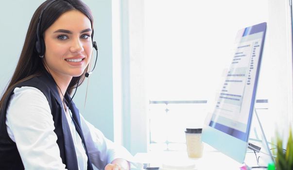 Businesswoman wearing microphone headset using computer in the office - operator, call center.