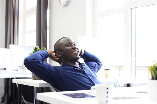 Relaxed Afro American business man sitting at his desk looking into the air