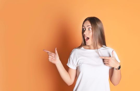 Young woman in basic clothing smiling and pointing finger at copyspace isolated on yellow background.