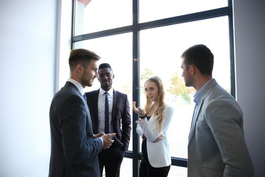 Group of young modern people in smart casual wear having a brainstorm meeting while standing in the creative office.