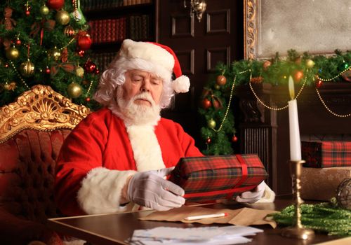 Portrait of happy Santa Claus sitting at his room at home near Christmas tree with gift box.