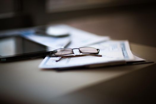 Glasses are on the documents and charts next to the tablet computer