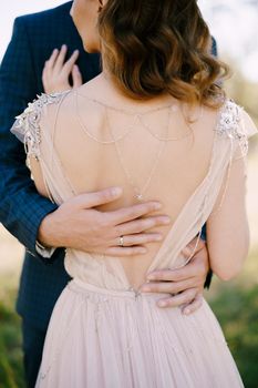 Groom hands hug bride lower back. Back view. Close-up. High quality photo