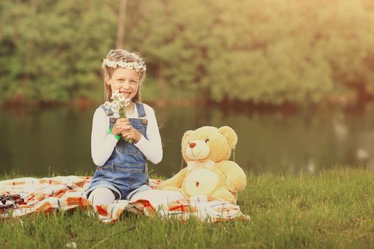 little girl with a soft toy on a picnic near the river on a Sunny day