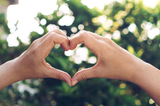 Woman hand do heart shape on green nature bokeh tropical background.