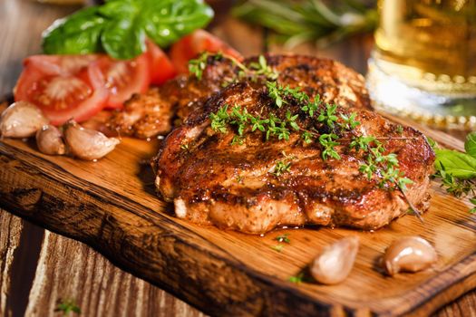  Fried pork steak on a wooden board to serve with vegetables and a mug of beer.