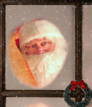 Santa Claus seen through the frosted window of his North Pole Workshop holding his Naughty and Nice List. It is snowing outside.