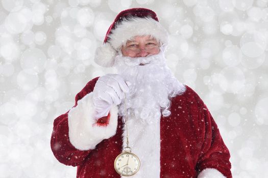 Closeup of Santa Claus holding a large gold pocket watch, with Bokeh background with snow effect.