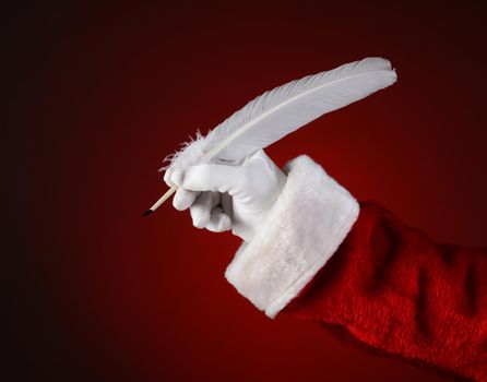 Closeup of Santa Claus holding a quill pen. Horizontal format on a light to dark red spot background.