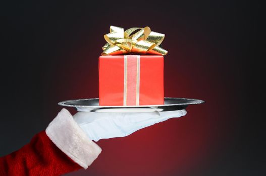 Santa Claus holding a tray with a wrapped present. Hand and arm only over a light to dark red background.