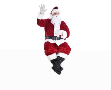 Senior man in traditional Santa Claus Suit sitting on a white wall with one hand in the air and the other on his belly and his eyes closed.  Isolated on white with copy space.