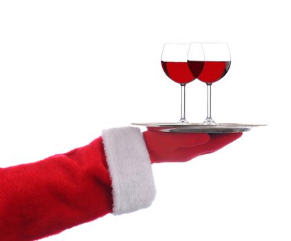 Santa Claus outstretched arm holding a silver serving tray with two glasses of red wine over a white background.