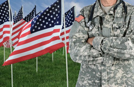 Closeup of a American Soldier / Medic in front of a large group of American Flags in a field of grass with a blue cloudy sky.