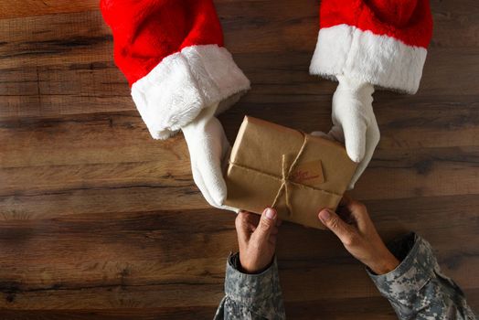 Santa Claus handing a plain wrapped Christmas Present to a soldier. High angle shot with only hands and arms visible.