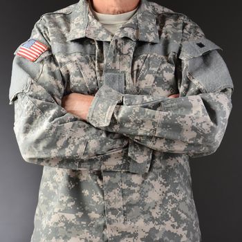 Closeup of a soldier wearing camouflage fatigues with his arms folded. Square format, man is unrecognizable.