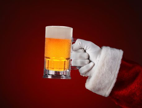 Closeup of Santa Claus holding a mug of beer. Horizontal format on a light to dark red spot background.