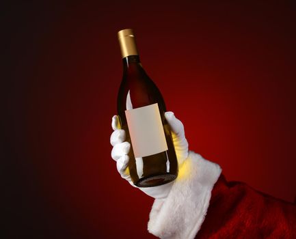 Closeup of Santa Claus holding a bottle of Chardonnay wine in his hand. Hand and arm only over a light to dark red spot background.