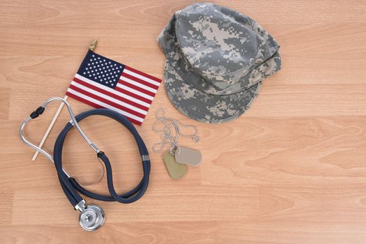 Military Health Care Concept. Light wood background with stethoscope, American flag, camo hat, and dog tags.