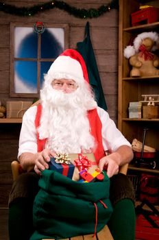 Santa Claus Sitting is a Rocking Chair with presents and toys in Bag. Vertical Composition - focus on Santa