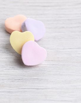 Closeup with shallow depth of field of 4 pastel Valentine's Day heart shaped candies on a white wood surface.