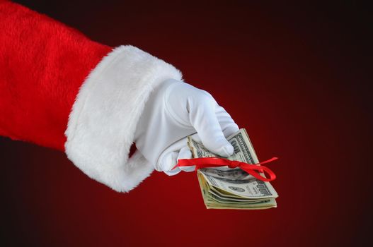 Santa Claus hand with cash tied up with a red ribbon. Horizontal format over a light to dark red background.