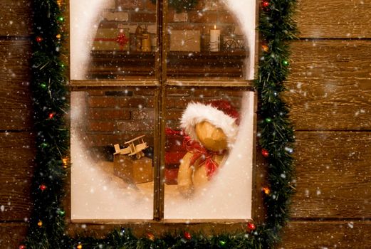 Looking through the frosty window of Santa Claus North Pole workshop with toys on work bench in front of brick fireplace. Horizontal with snow effect.