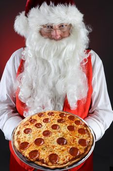 Santa Claus serving a fresh homemade pepperoni pizza. He is holding the platter in both hands in front of his torso. 