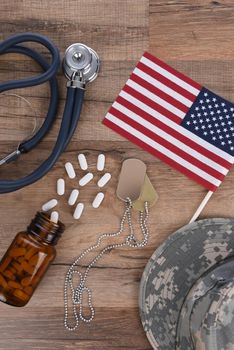Military Health Care Concept. Dog tags, stethoscope, pills, camouflage hat and American Flag on a wood background. 