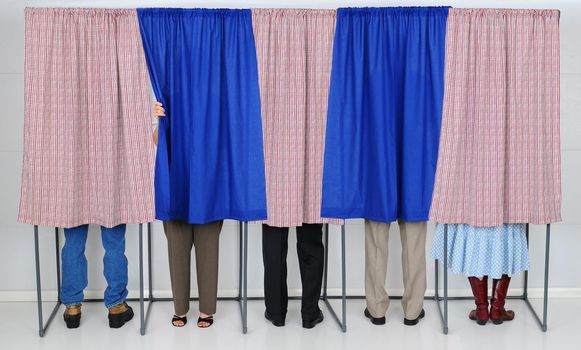 A row of five voting booths with men and women casting their ballots at a polling place. Horizontal format, only showing the legs of the voters, people are unrecognizable..
