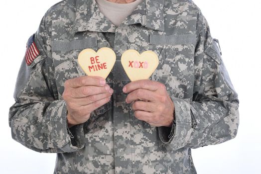 Closeup of a soldier holding two Heart Shaped Valentines Day cookies with the words Be Mine and XOXO written in red icing.