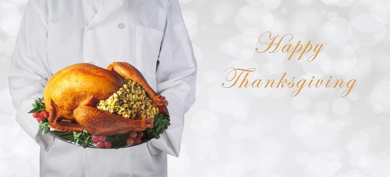 Chef holding a Thanksgiving turkey on a platter over a  silver bokeh background, with Happy Thanksgiving and copy space.