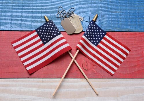 Two crossed American flags on a red, white and blue wood table with military dog tags. Great concept image for the 4th of July, Memorial Day,  Veterans Day or military projects.