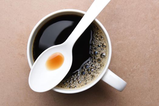 Top view of a plastic spoon laying across the top of a white coffee mug. 