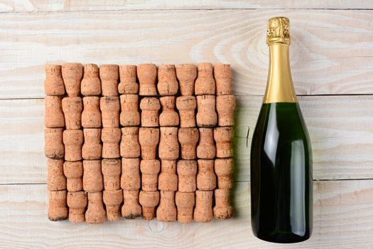 High angle shot of a bottle of champagne laying next to a large group of corks arranged in rows on a whitewashed wood table. 