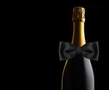 Closeup of an unopened bottle of Champagne against a black background with Black Bow Tie. Ideal for Wedding, Anniversary or New Years Projects, with copy space. 