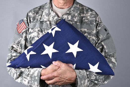 Closeup of an American Soldier in fatigues holding a folded flag in front of his torso. The man is unrecognizable.