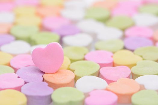 Closeup of a pink candy heart for Valentines Day standing out in a field of out of focus similar candies. Heart is set to one side leaving room for your copy. The candies are blank.
