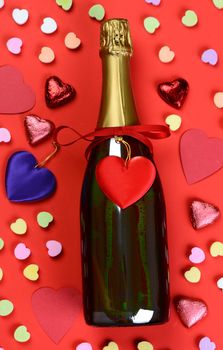 A bottle of Champagne surrounded by hearts and assorted Valentines Day candy.