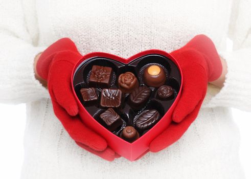Closeup of a Valentines Day heart shaped box filled with chocolates. Vignette added as unrecognizable woman holds the box in front of her torso.