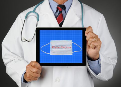 Closeup of a doctor holding a tablet computer with a Surgical mask and Flatten the Curve